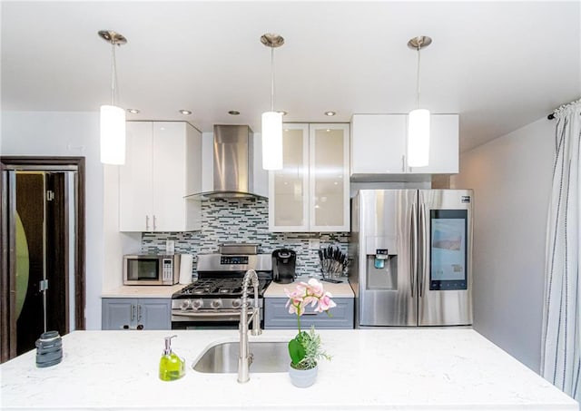 kitchen with stainless steel appliances, hanging light fixtures, wall chimney range hood, and white cabinets