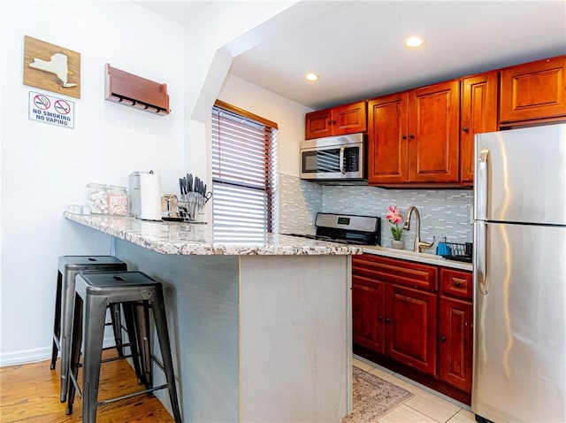 kitchen featuring sink, light stone countertops, a kitchen bar, decorative backsplash, and stainless steel appliances