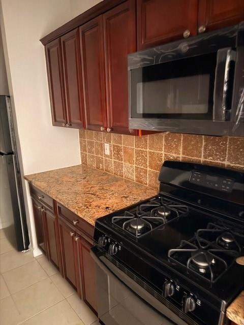 kitchen with light tile patterned floors, freestanding refrigerator, black gas range oven, backsplash, and light stone counters