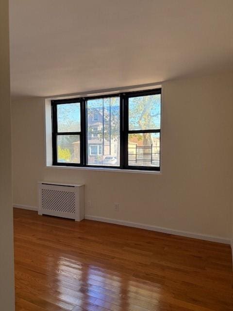 empty room featuring radiator, wood finished floors, and baseboards