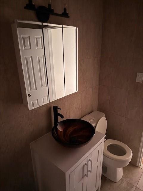 half bath with tile patterned flooring, vanity, tile walls, and toilet