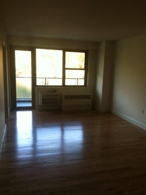 spare room with a wall mounted air conditioner, radiator, and dark wood-type flooring