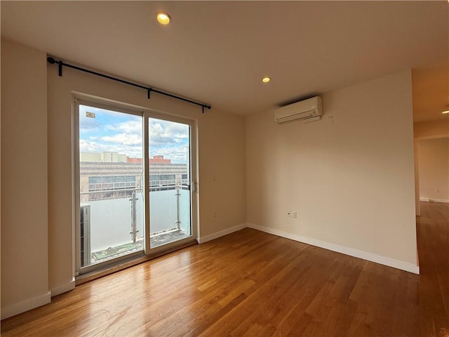 spare room with wood finished floors, baseboards, and a wall mounted air conditioner