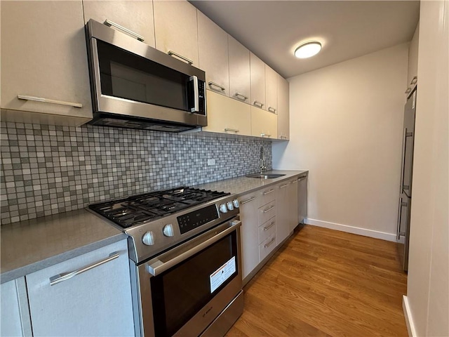 kitchen featuring a sink, light wood-style floors, appliances with stainless steel finishes, decorative backsplash, and baseboards