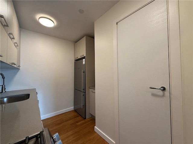 kitchen with baseboards, a sink, dark wood-type flooring, white cabinetry, and stainless steel fridge