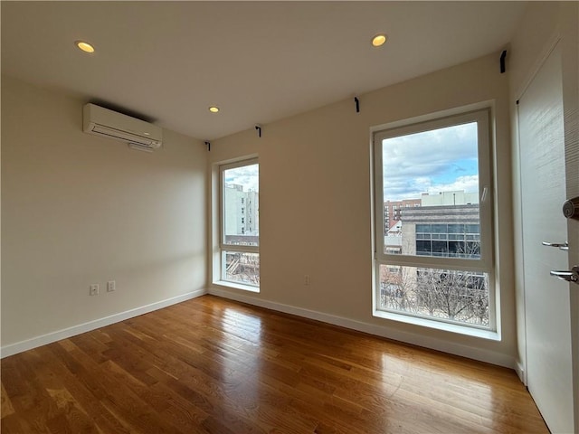 spare room with baseboards, a wall unit AC, wood finished floors, and recessed lighting