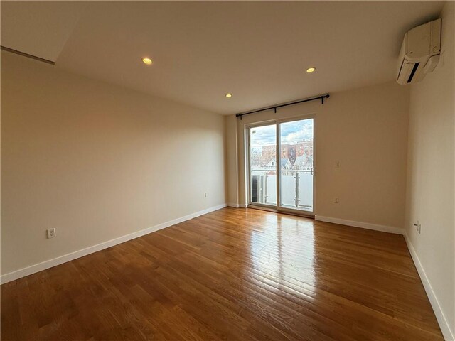 empty room featuring recessed lighting, baseboards, wood finished floors, and a wall mounted AC