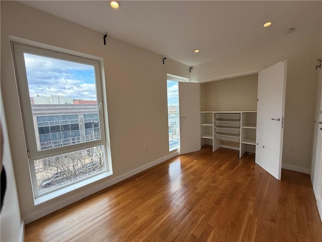 unfurnished bedroom featuring recessed lighting, baseboards, multiple windows, and wood finished floors