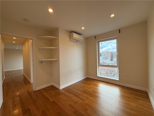 empty room with recessed lighting, a wall mounted AC, baseboards, and wood finished floors