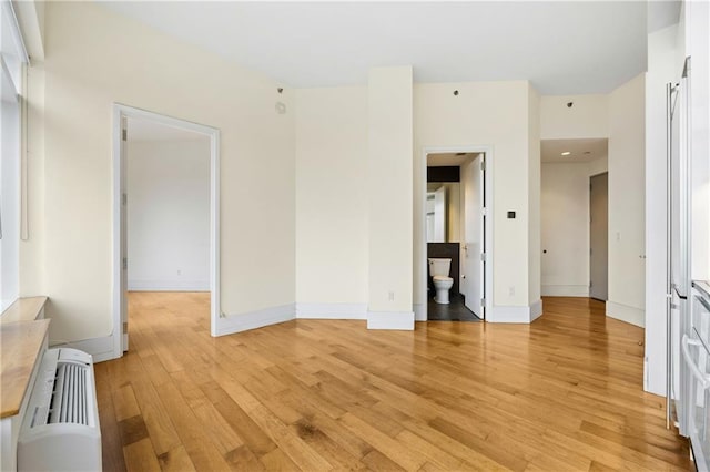 empty room with radiator, light wood-style flooring, and baseboards