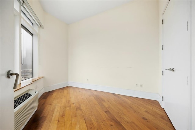 unfurnished bedroom with light wood-style flooring, baseboards, and an AC wall unit