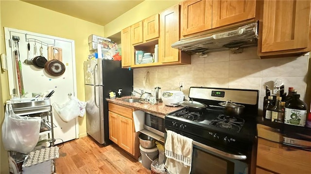 kitchen featuring backsplash, sink, light stone countertops, gas range oven, and stainless steel refrigerator