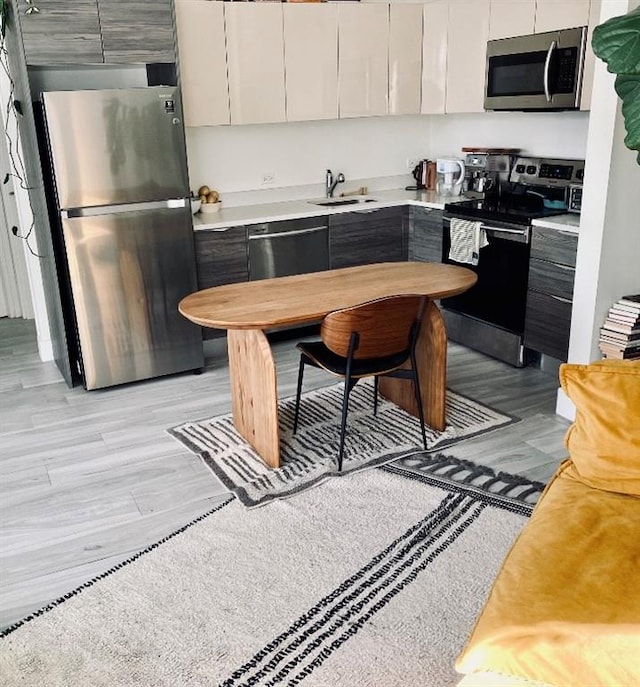 kitchen featuring appliances with stainless steel finishes, light hardwood / wood-style flooring, white cabinetry, and sink