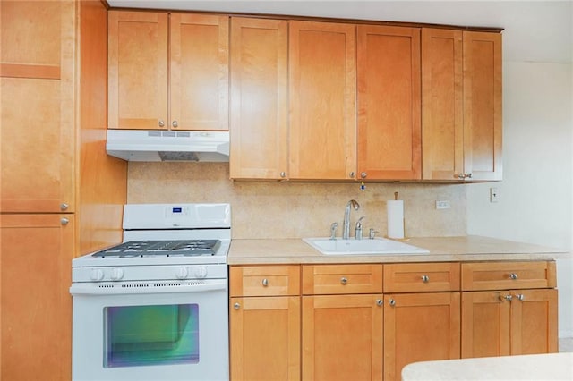 kitchen with tasteful backsplash, gas range gas stove, under cabinet range hood, light countertops, and a sink