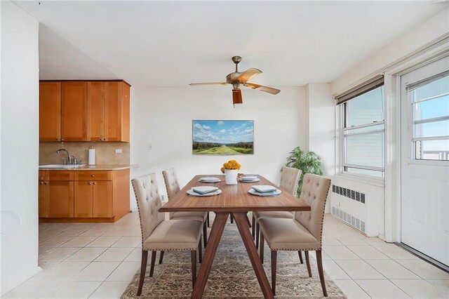 tiled dining room with ceiling fan, radiator, and sink