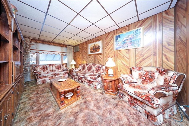 carpeted living room featuring a drop ceiling and wooden walls