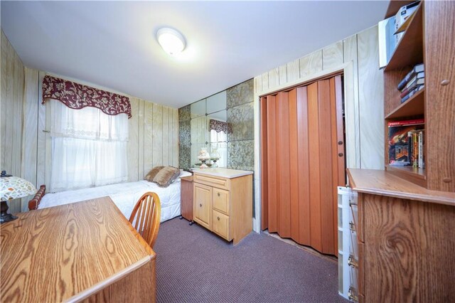 carpeted bedroom with a closet and wood walls