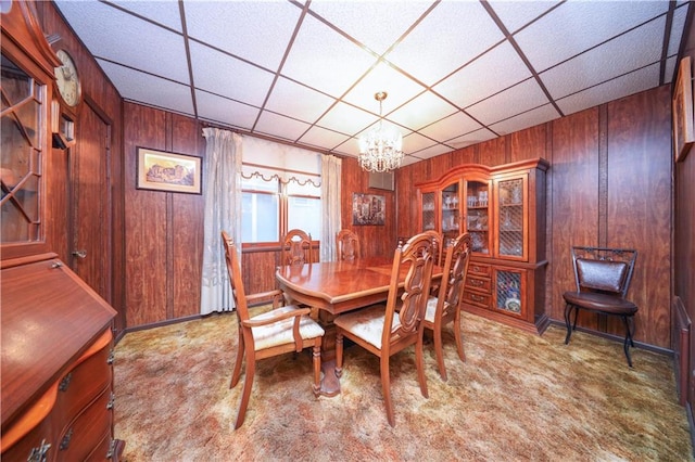 carpeted dining space featuring a paneled ceiling, a chandelier, and wood walls