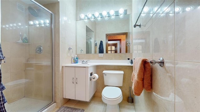 bathroom featuring walk in shower, tile patterned floors, toilet, vanity, and tile walls