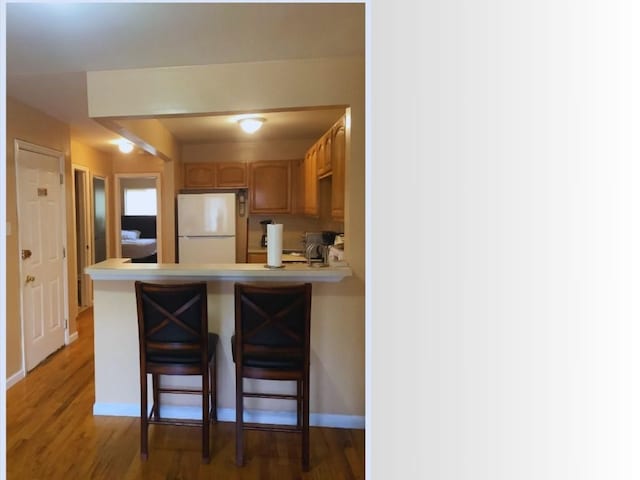 kitchen with kitchen peninsula, a kitchen bar, white fridge, and dark hardwood / wood-style floors