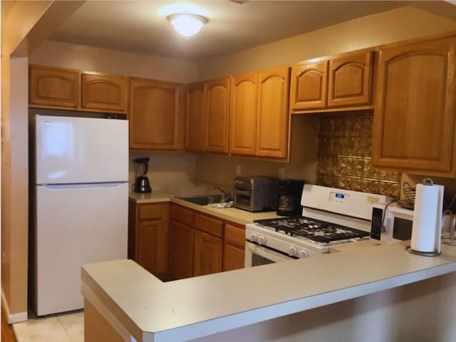 kitchen with decorative backsplash, light tile patterned floors, white appliances, and sink