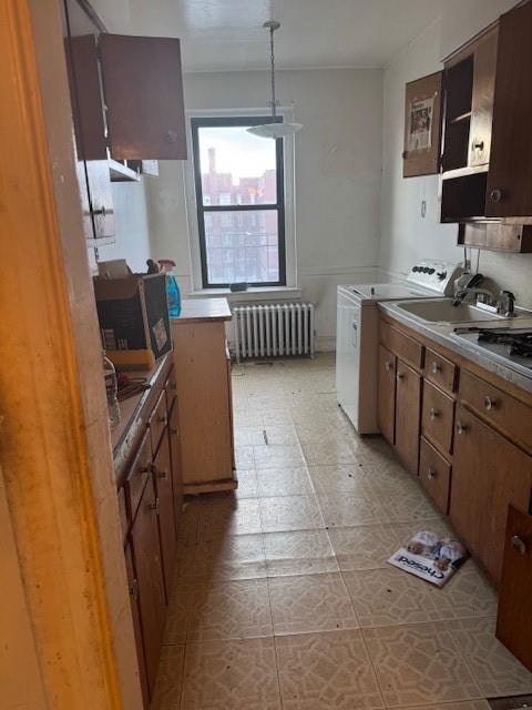 kitchen with radiator heating unit, hanging light fixtures, light countertops, brown cabinets, and stainless steel microwave