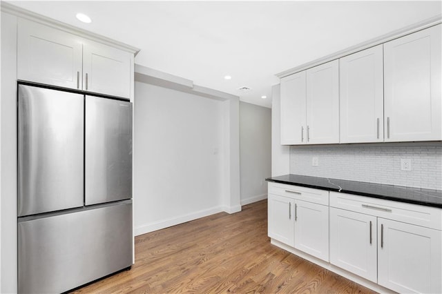 kitchen with white cabinetry, tasteful backsplash, stainless steel refrigerator, dark stone counters, and light hardwood / wood-style floors