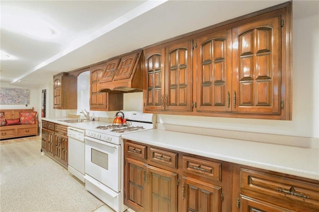 kitchen with a sink, white appliances, custom exhaust hood, and brown cabinets