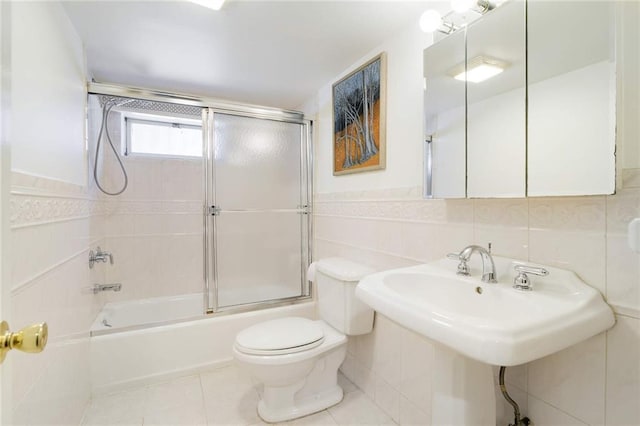 full bath featuring bath / shower combo with glass door, tile patterned flooring, wainscoting, tile walls, and toilet