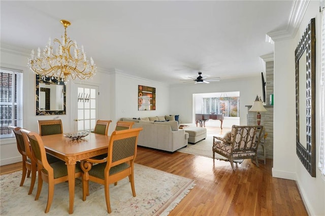 dining space with ceiling fan with notable chandelier, crown molding, baseboards, and wood finished floors