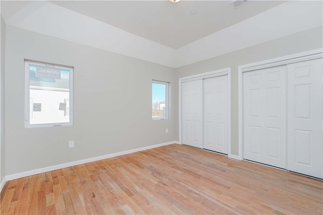 unfurnished bedroom featuring multiple windows, baseboards, light wood-type flooring, and two closets