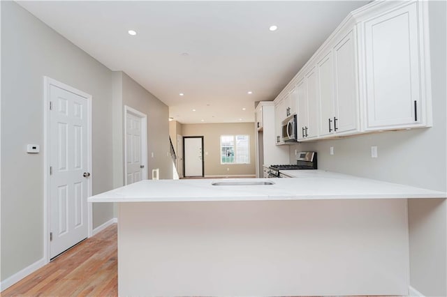 kitchen with light wood-type flooring, white cabinetry, stainless steel appliances, a peninsula, and light countertops