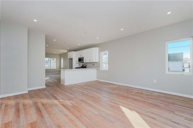 unfurnished living room with light wood finished floors, recessed lighting, and baseboards