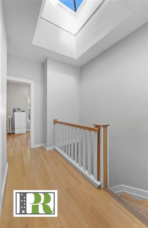 hall with a skylight, wood-type flooring, baseboards, and an upstairs landing