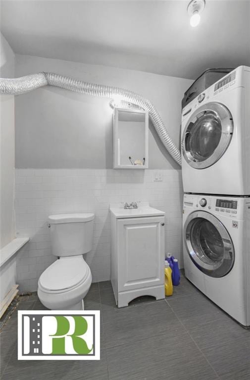 laundry room with stacked washer and dryer, dark tile patterned flooring, laundry area, and tile walls