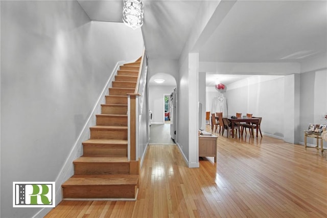 foyer entrance featuring arched walkways, light wood-type flooring, stairway, and baseboards