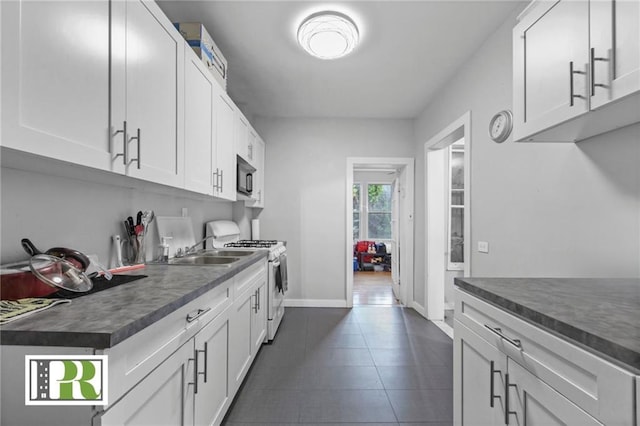 kitchen with black microwave, white gas stove, dark tile patterned flooring, white cabinets, and dark countertops