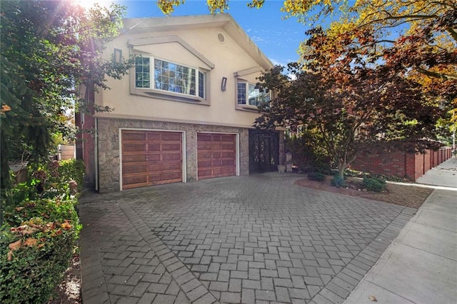 traditional home featuring a garage, stone siding, decorative driveway, and stucco siding