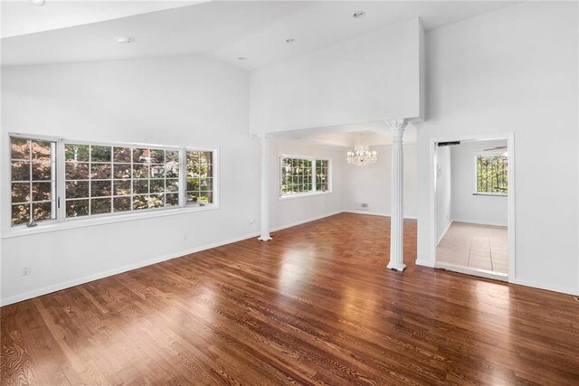 unfurnished living room featuring an inviting chandelier, a wealth of natural light, high vaulted ceiling, and hardwood / wood-style flooring