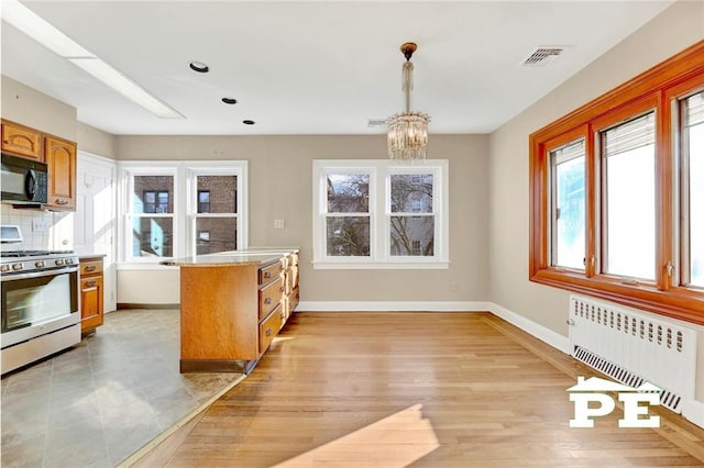 kitchen with radiator, hanging light fixtures, tasteful backsplash, a notable chandelier, and stainless steel range with gas cooktop