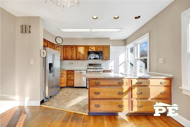 kitchen featuring stainless steel appliances, kitchen peninsula, decorative backsplash, and light hardwood / wood-style flooring