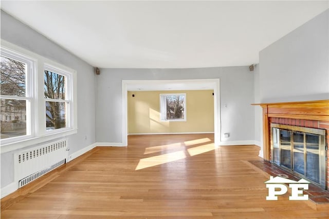 unfurnished living room with radiator heating unit, light hardwood / wood-style floors, and a brick fireplace