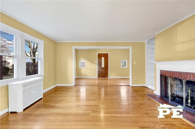 unfurnished living room with built in shelves, radiator heating unit, crown molding, and light wood-type flooring