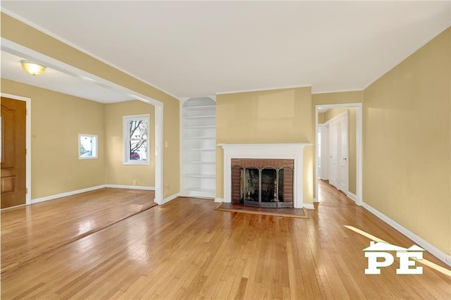 unfurnished living room featuring built in shelves, ornamental molding, wood-type flooring, and a fireplace