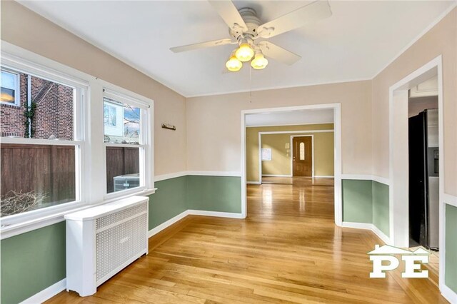 unfurnished room featuring radiator, ceiling fan, and light hardwood / wood-style flooring