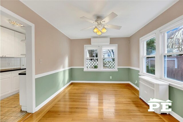 unfurnished room with an AC wall unit, ceiling fan, and light hardwood / wood-style flooring