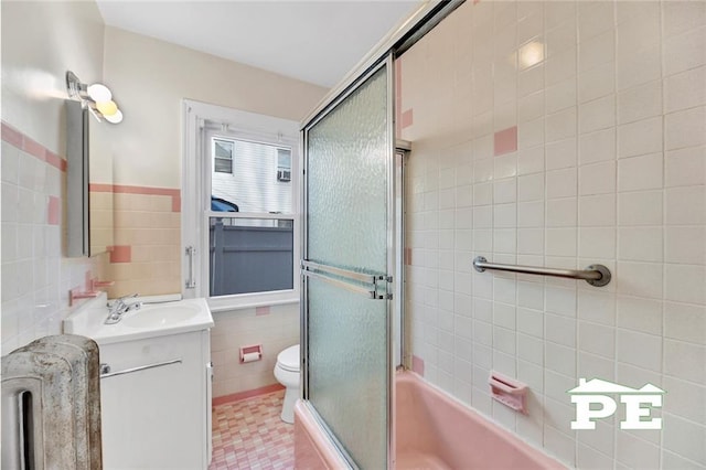 full bathroom with toilet, combined bath / shower with glass door, tile walls, radiator heating unit, and vanity