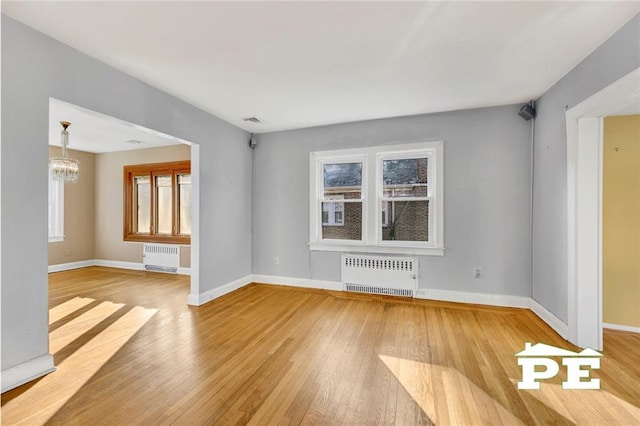 unfurnished living room featuring radiator, a chandelier, and light wood-type flooring