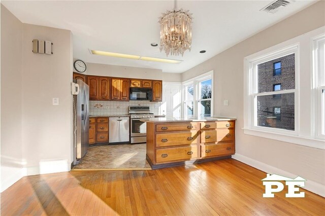 kitchen featuring light wood-type flooring, appliances with stainless steel finishes, a notable chandelier, pendant lighting, and decorative backsplash