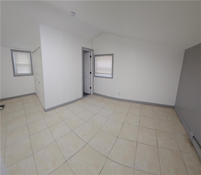 tiled empty room with vaulted ceiling and a baseboard heating unit